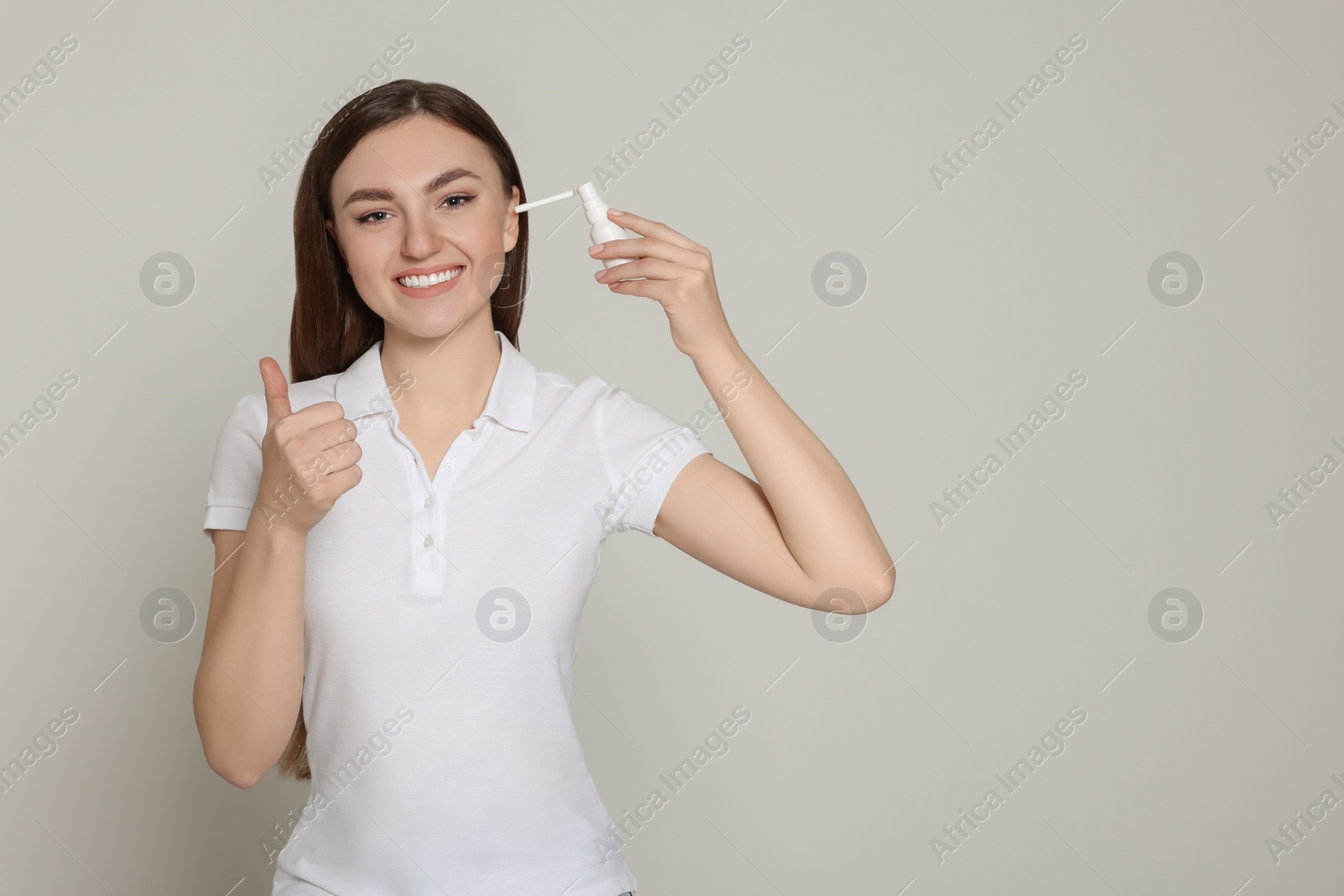 Photo of Woman using ear spray and showing thumbs up on light grey background. Space for text