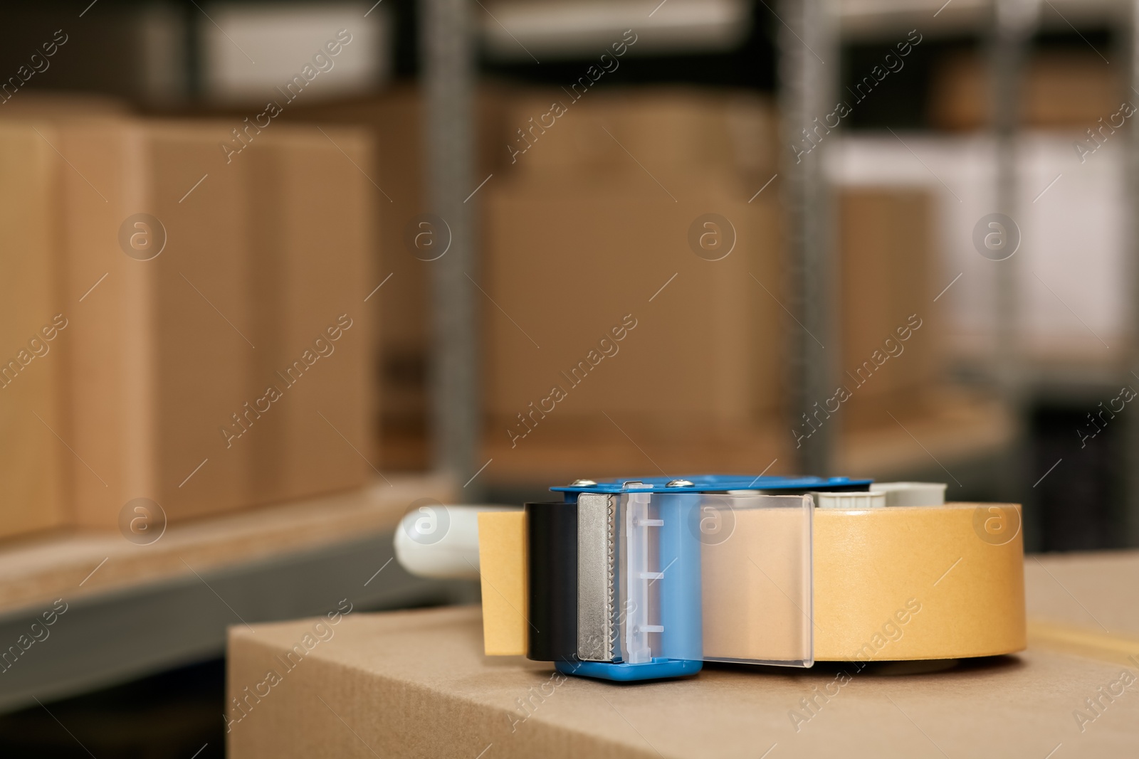 Photo of Adhesive tape dispenser on cardboard box indoors. Space for text