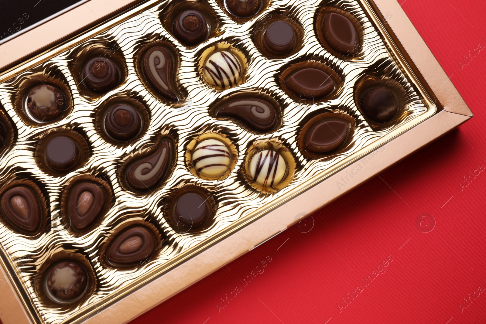 Photo of Box of delicious chocolate candies on red background, top view