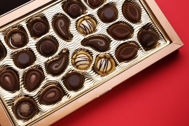 Box of delicious chocolate candies on red background, top view