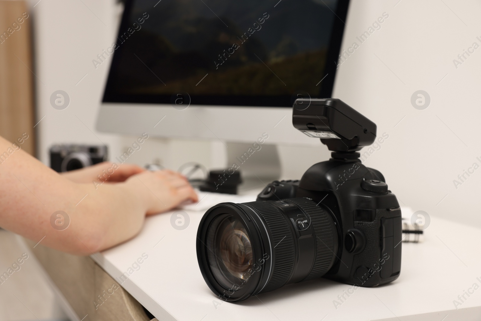 Photo of Photographer working on computer at white table with camera indoors, closeup