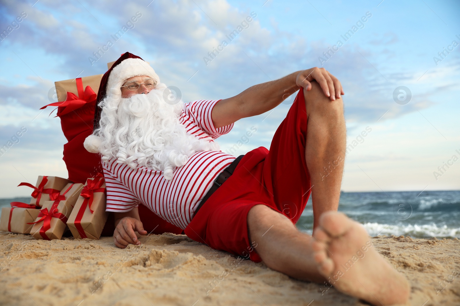 Photo of Santa Claus with bag of presents relaxing on beach. Christmas vacation