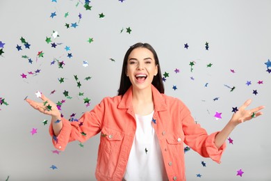 Photo of Emotional woman and falling confetti on light grey background