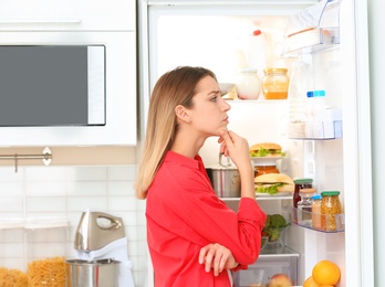 Photo of Thoughtful young woman choosing food from refrigerator in kitchen. Healthy diet