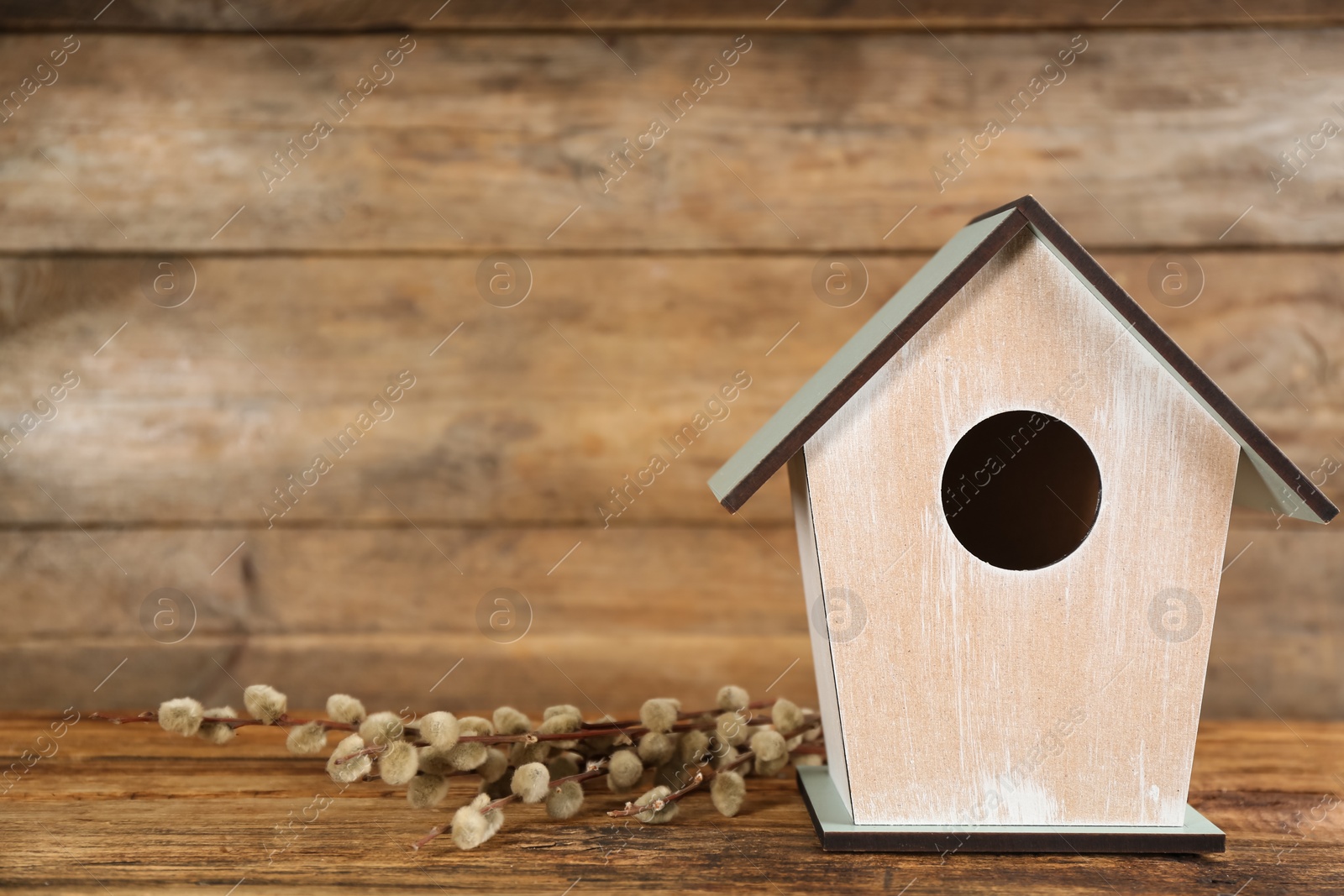 Photo of Beautiful bird house and pussy willow branches on wooden table, space for text