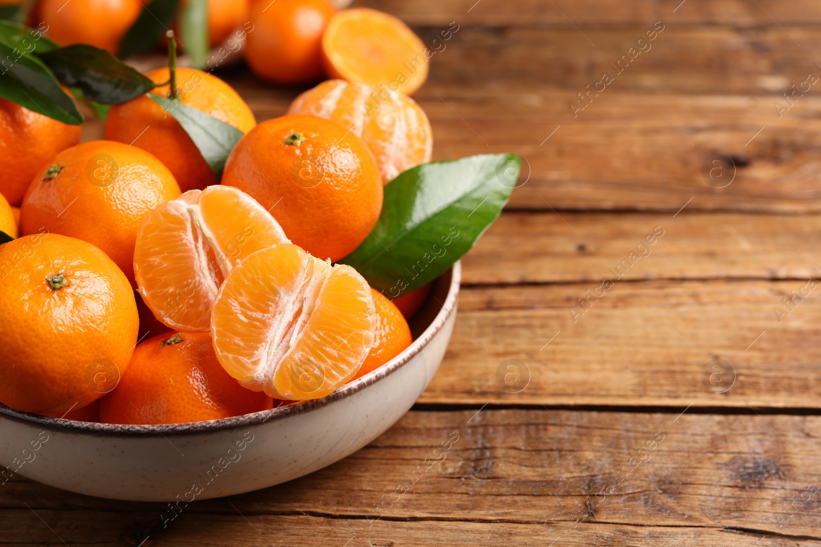 Photo of Fresh tangerines with green leaves in bowl on wooden table, closeup. Space for text