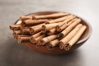 Photo of Aromatic cinnamon sticks in bowl on grey stone table, closeup
