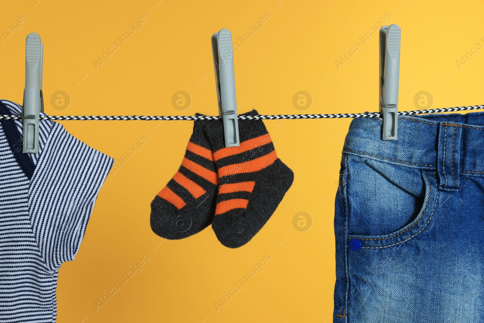 Photo of Different baby clothes drying on laundry line against orange background, closeup