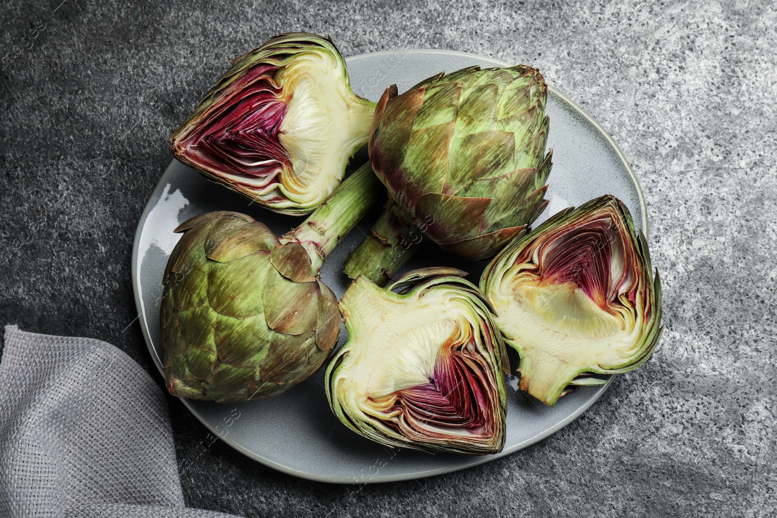 Photo of Cut and whole fresh raw artichokes on grey table, top view