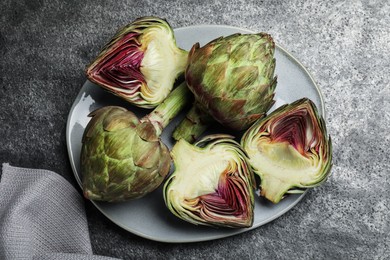 Cut and whole fresh raw artichokes on grey table, top view