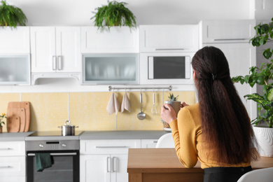 Woman with drink at table in kitchen decorated with plants. Home design