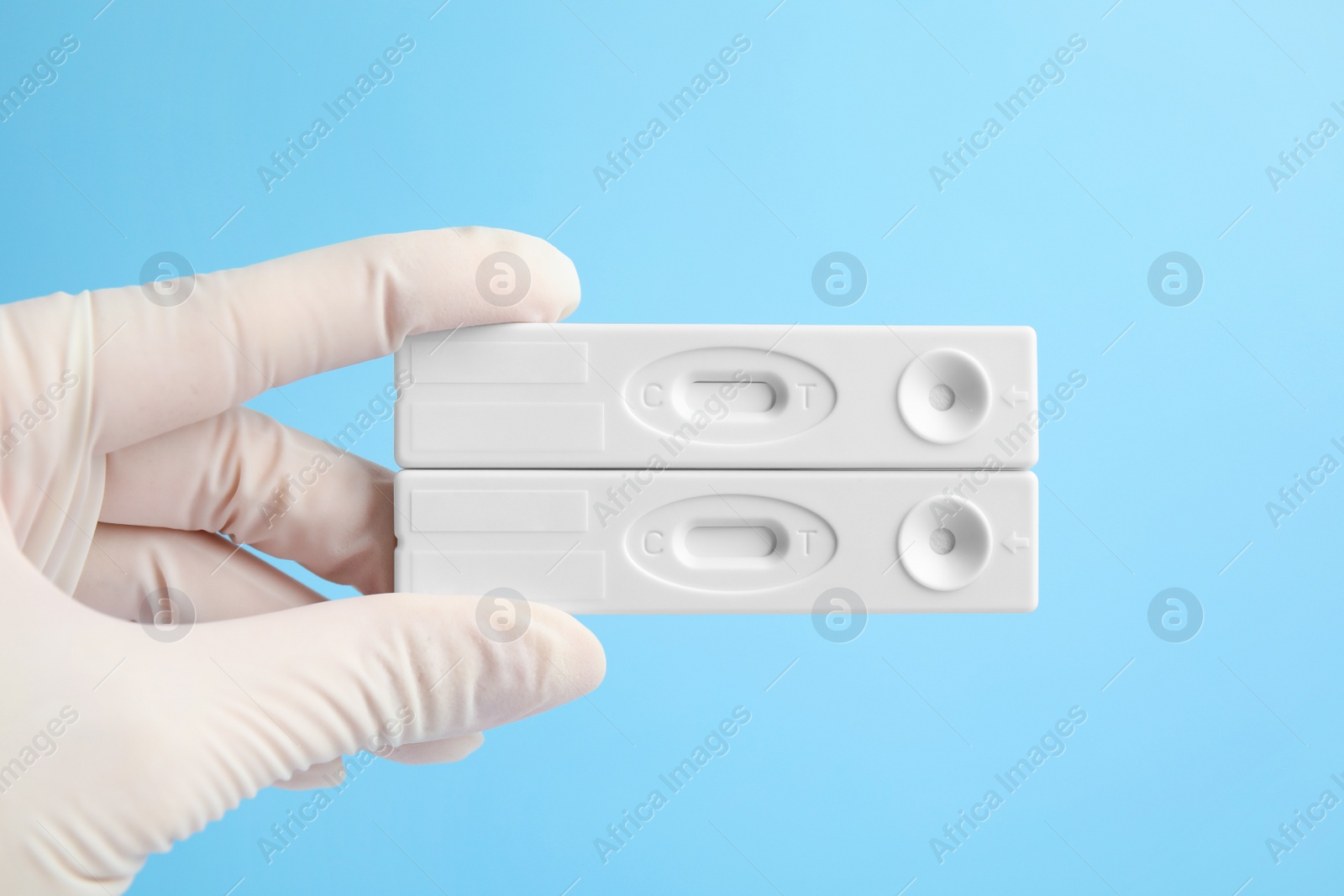 Photo of Doctor holding two disposable express tests for hepatitis on light blue background, closeup