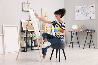 Photo of Young woman painting on easel with canvas in studio