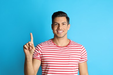 Man showing number one with his hand on light blue background