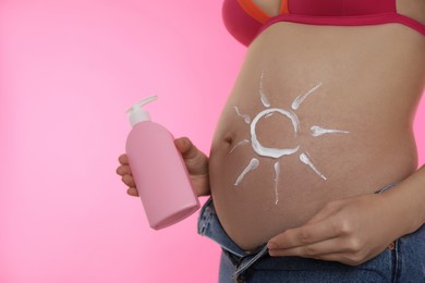 Photo of Young pregnant woman with sun protection cream on pink background, closeup. Space for text