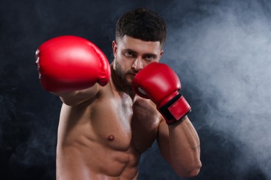 Man wearing boxing gloves fighting in smoke on black background