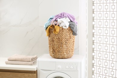 Photo of Wicker basket with dirty clothes on washing machine in bathroom