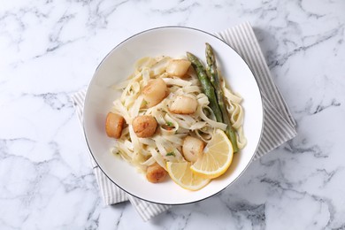 Photo of Delicious scallop pasta with asparagus and lemon on white marble table, top view