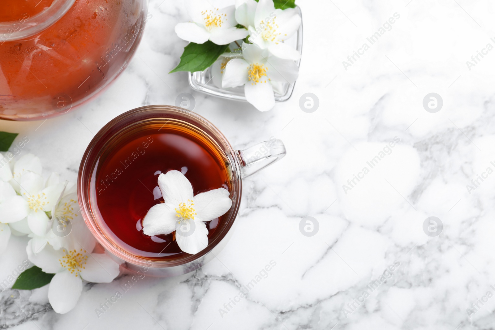 Photo of Cup of tea and fresh jasmine flowers on white marble table, flat lay. Space for text