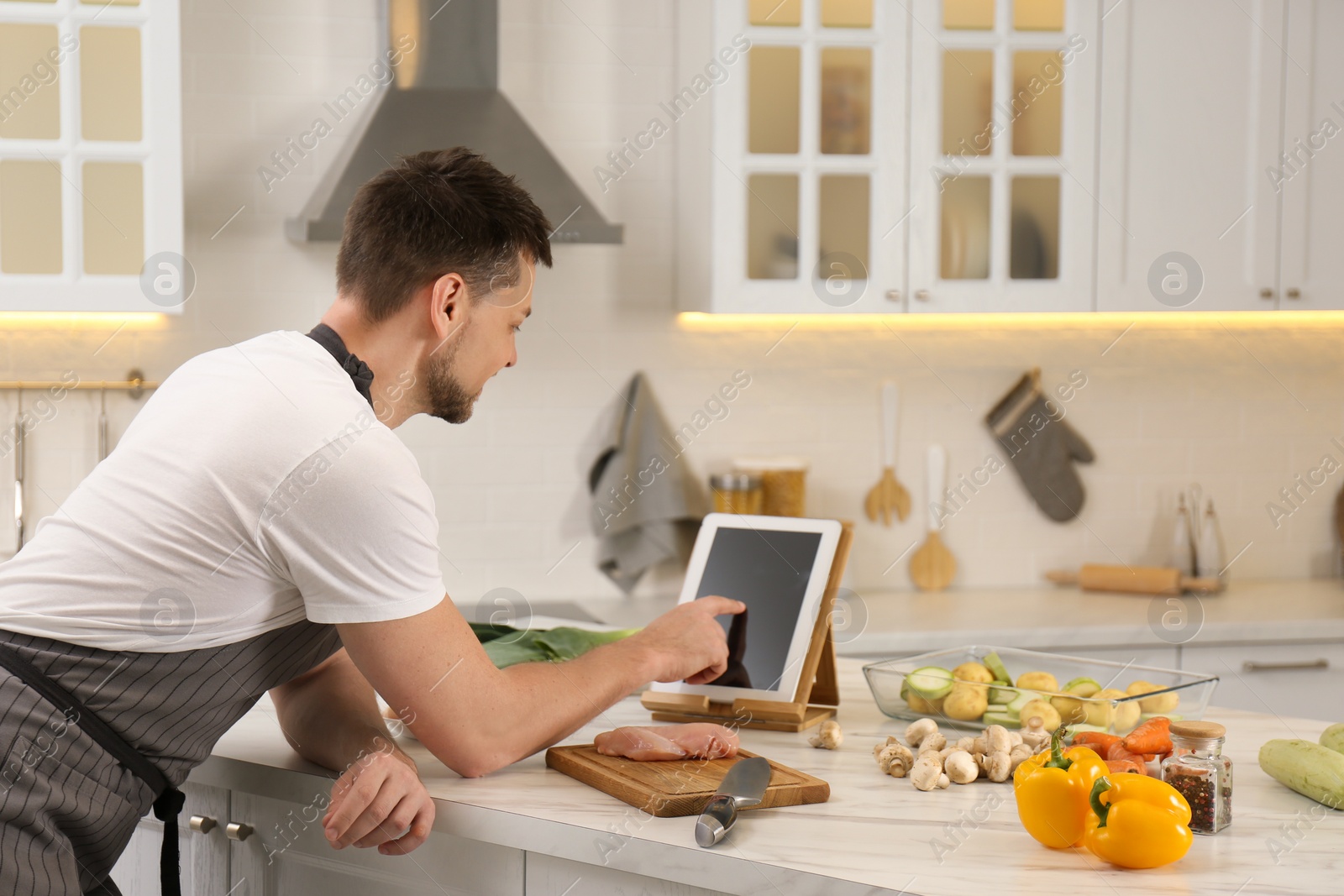 Photo of Man making dinner while watching online cooking course via tablet in kitchen