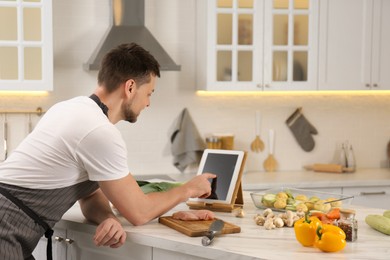 Man making dinner while watching online cooking course via tablet in kitchen