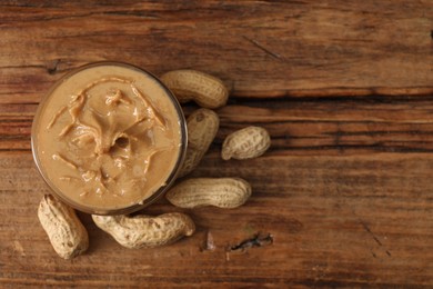 Photo of Delicious nut butter in bowl and peanuts on wooden table, top view. Space for text