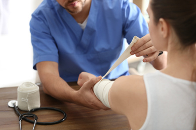 Photo of Male orthopedist applying bandage onto patient's elbow at table, closeup