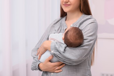 Mother holding her cute newborn baby indoors, closeup. Space for text