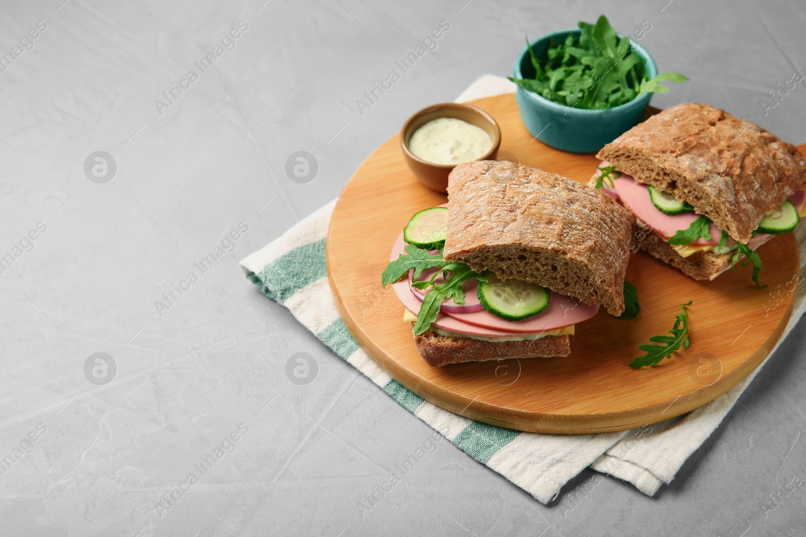 Photo of Tasty sandwiches with boiled sausage, cucumber, arugula and sauce on grey table. Space for text