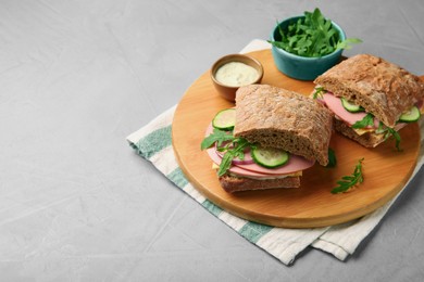 Tasty sandwiches with boiled sausage, cucumber, arugula and sauce on grey table. Space for text