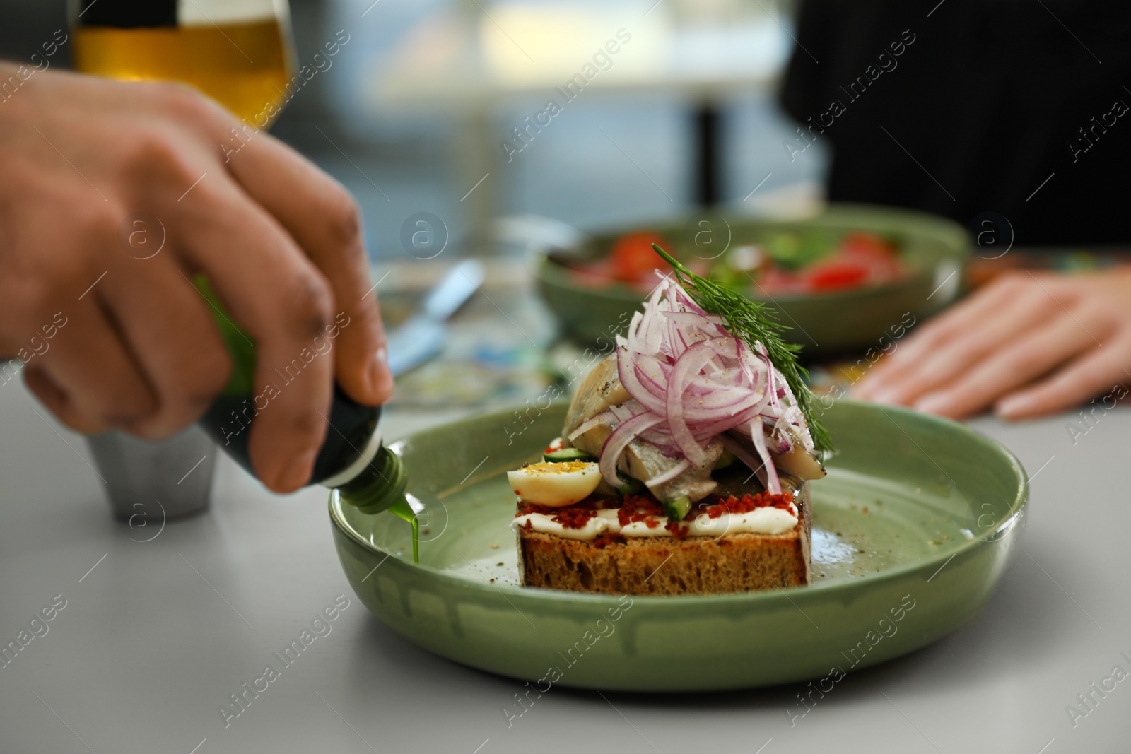 Photo of Man adding sauce to fish sandwich indoors, closeup
