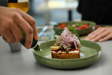 Man adding sauce to fish sandwich indoors, closeup