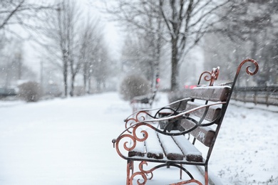 Photo of Bench covered with fresh snow on storm day in city park. Space for text