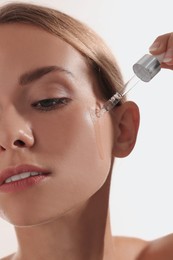 Woman applying cosmetic serum onto her face on white background, closeup