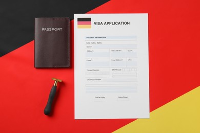 Immigration to Germany. Visa application form, stamp and passport on flag, flat lay