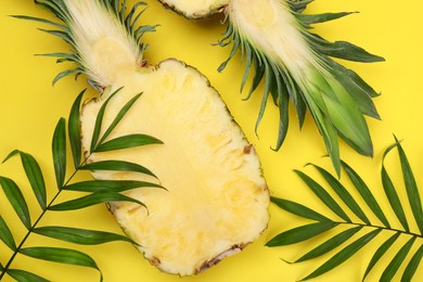 Photo of Halves of ripe pineapple and green leaves on yellow background, flat lay
