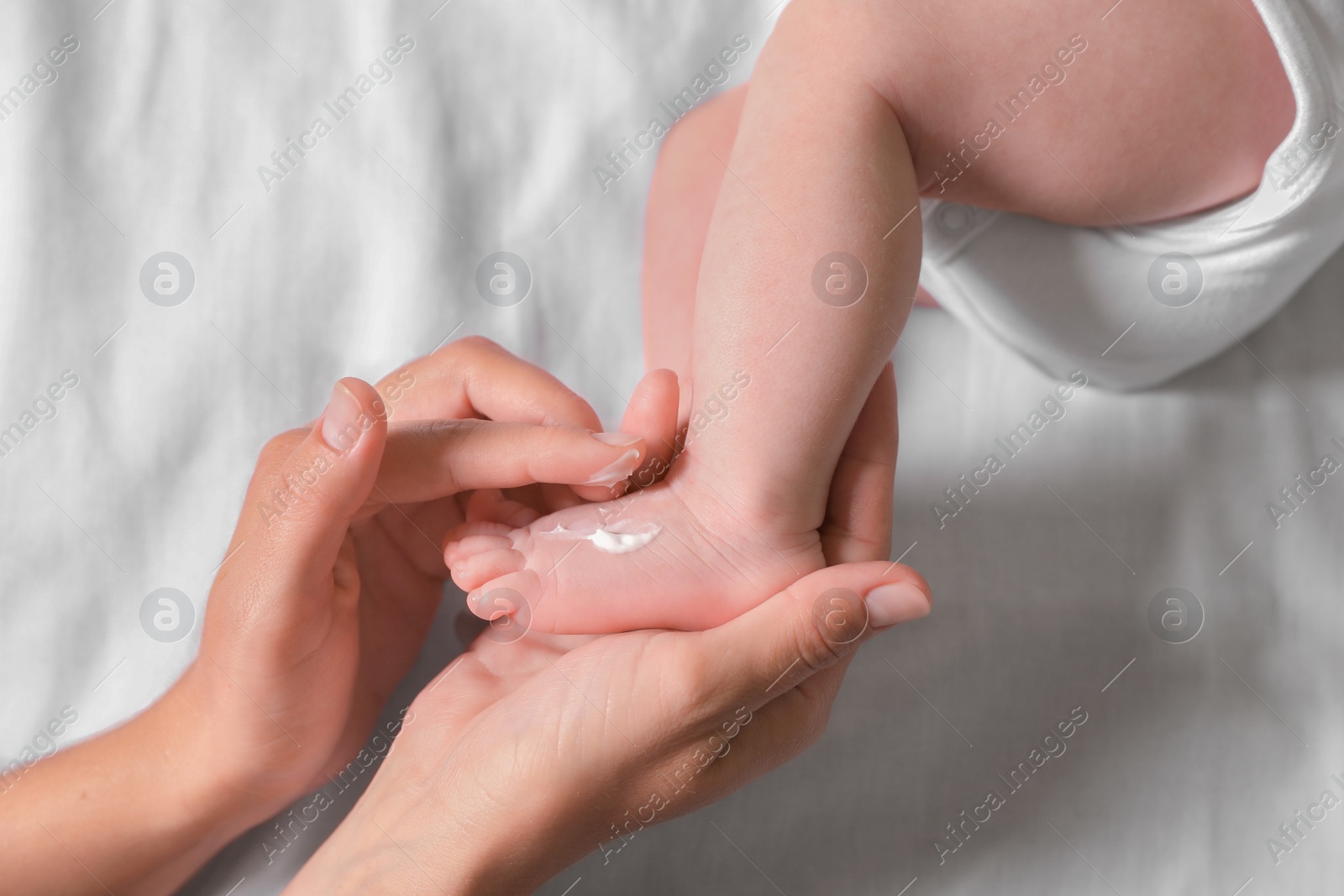 Photo of Mother applying moisturizing cream onto baby`s foot on bed, top view