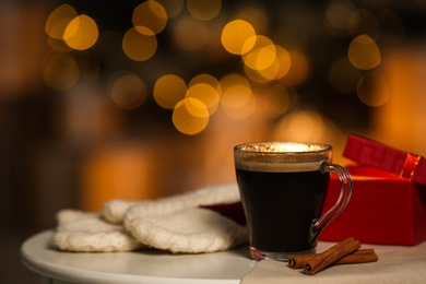 Photo of Cup of hot coffee on white table against blurred lights, space for text. Cozy winter