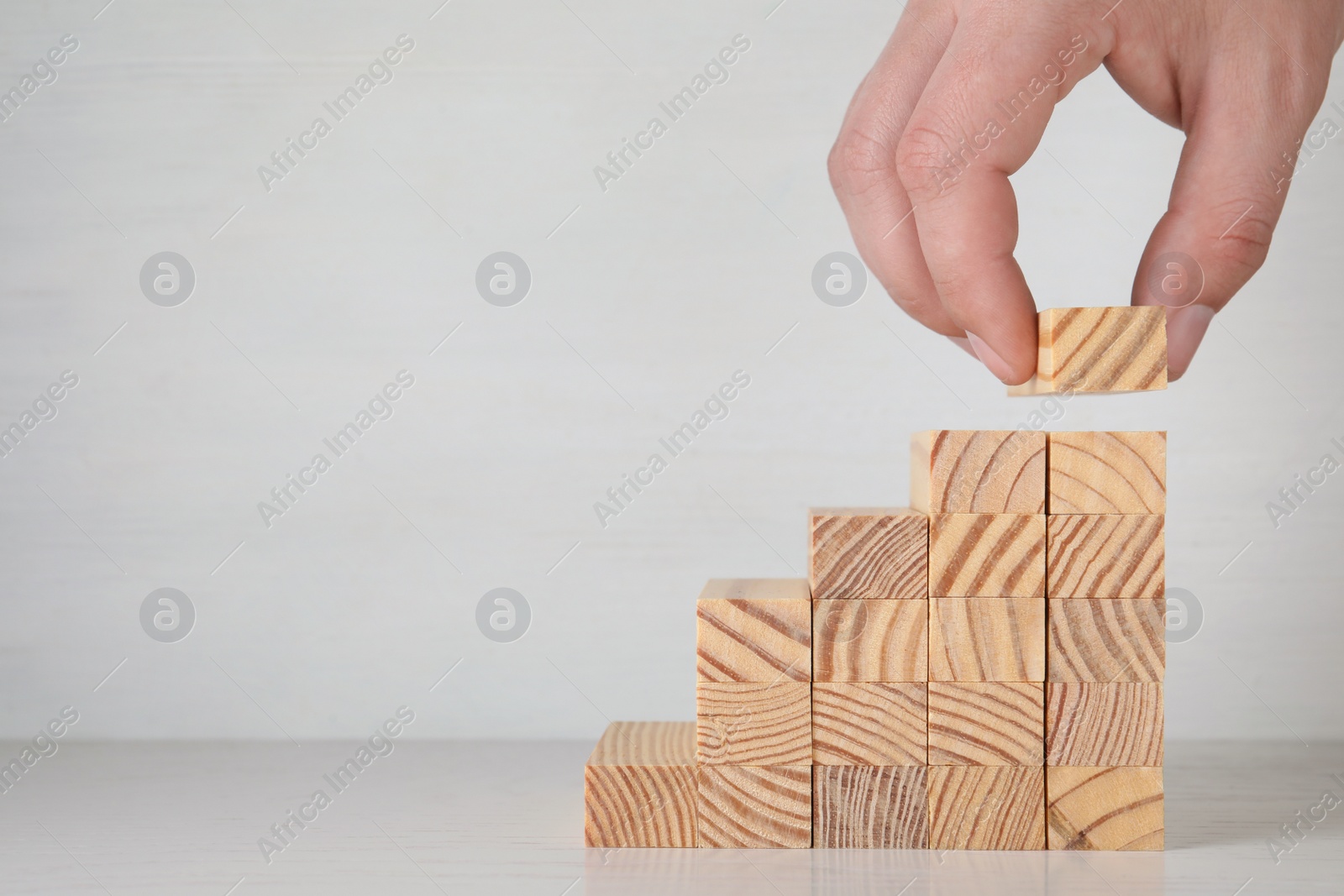 Photo of Closeup view of man building steps with wooden blocks on table against light background, space for text. Career ladder