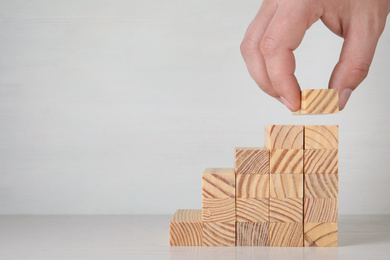 Photo of Closeup view of man building steps with wooden blocks on table against light background, space for text. Career ladder