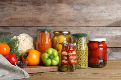 Photo of Glass jars with pickled vegetables on wooden table against brown background