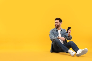 Happy man with smartphone on yellow background. Space for text