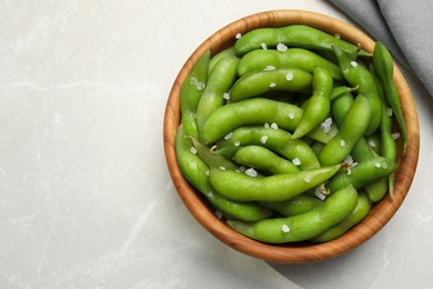 Photo of Bowl of green edamame beans in pods with salt on light grey table, top view. Space for text