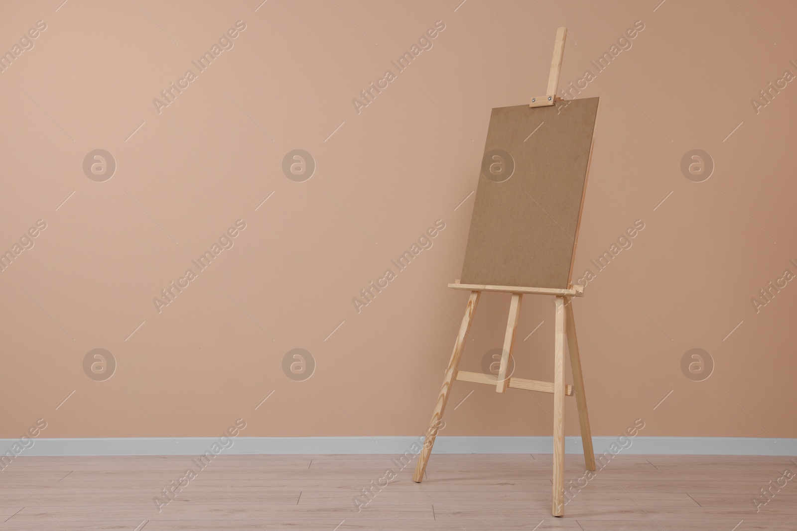 Photo of Wooden easel with blank board near beige wall indoors. Space for text