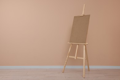 Wooden easel with blank board near beige wall indoors. Space for text