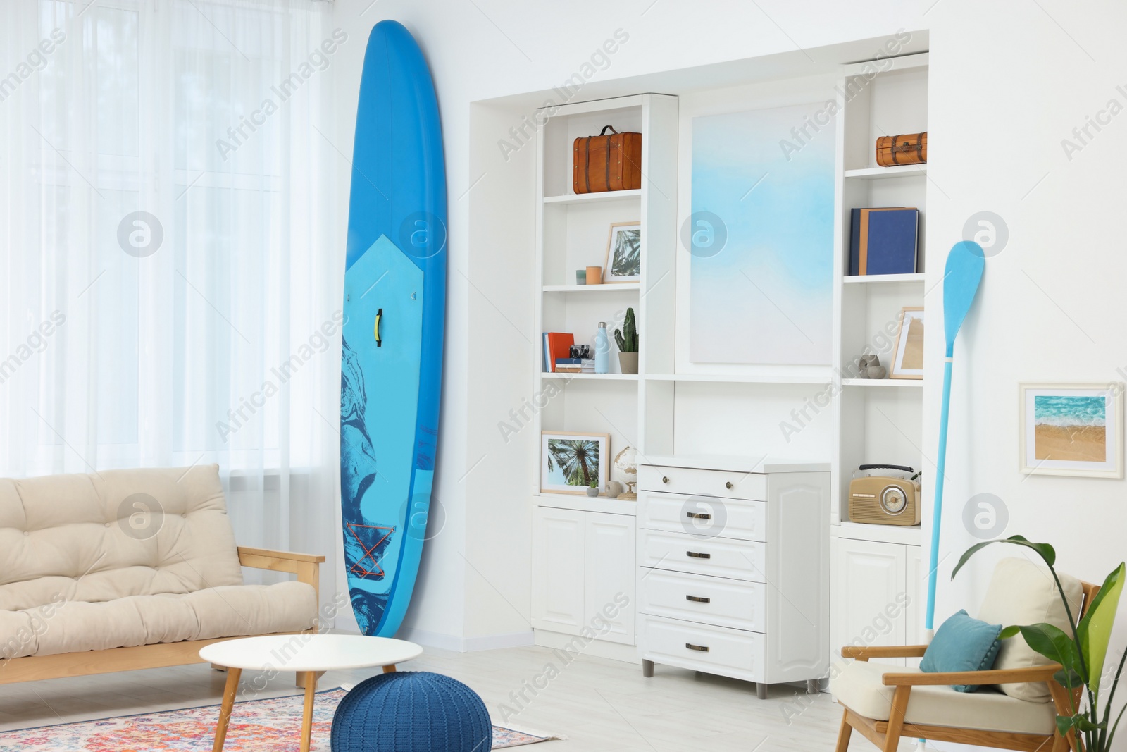 Photo of SUP board and modern furniture in stylish living room. Interior design