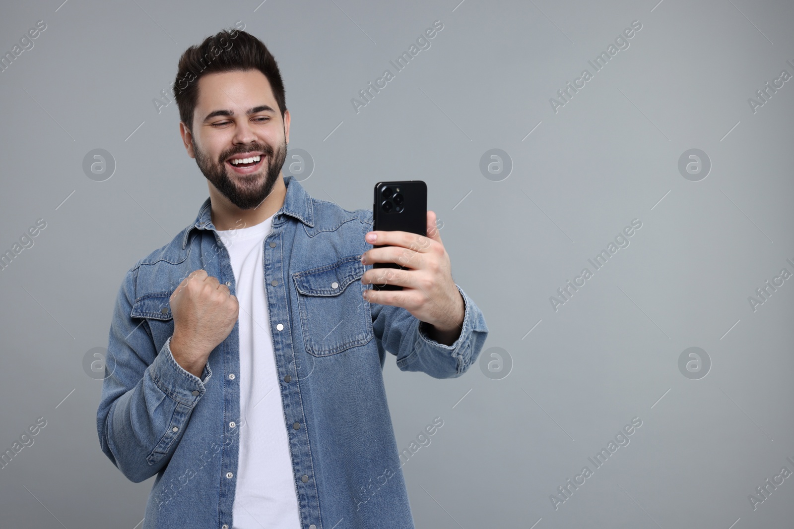 Photo of Happy young man using smartphone on grey background, space for text