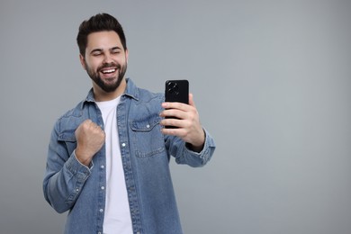 Happy young man using smartphone on grey background, space for text