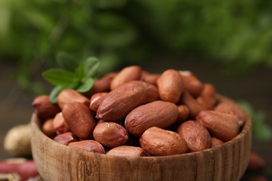 Photo of Fresh unpeeled peanuts in bowl on blurred green background, closeup