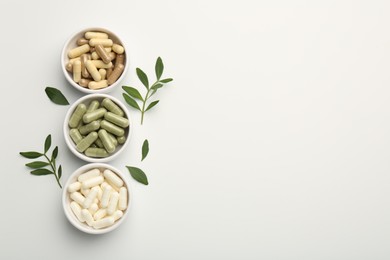 Photo of Different vitamin capsules in bowls and leaves on white background, flat lay. Space for text